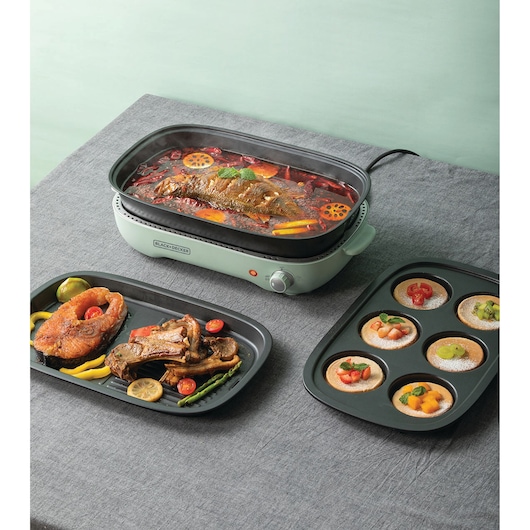 BLACK+DECKER GMF1400 electric grill with a whole fish cooking, surrounded by two trays with assorted grilled foods and desserts.