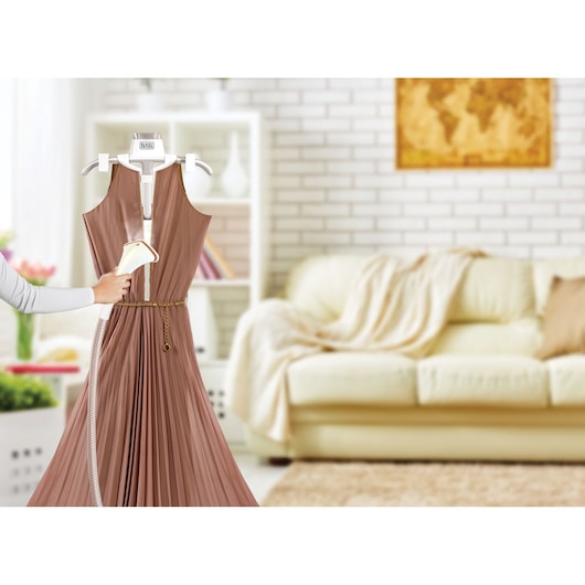 Photo of BLACKDECKER GST1600 garment steamer in use on a pleated brown dress in a bright living room.
