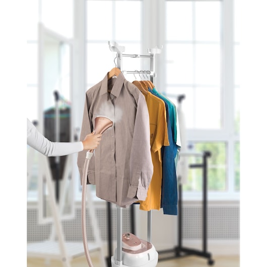 BLACKDECKER GSTD2050 garment steamer in use steaming shirts on rack, indoor setting.