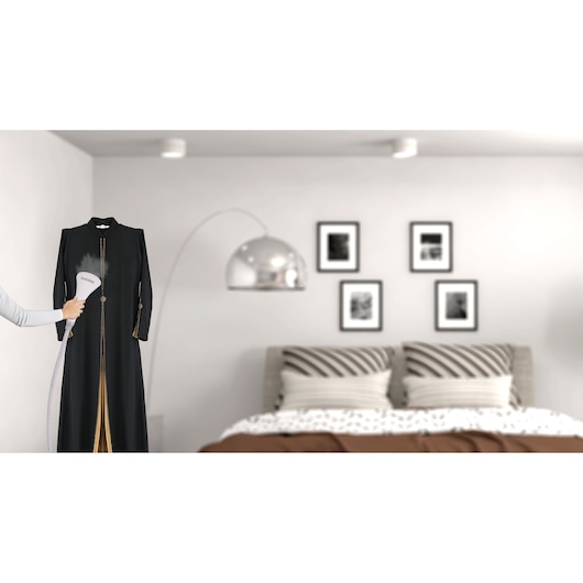 BLACKDECKER GSTM2050 handheld garment steamer in use, steaming a black dress in a modern bedroom.