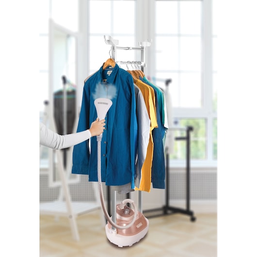 BLACKDECKER GSTM2050 garment steamer in use on blue shirt, several colorful shirts hanging on rack.
