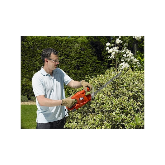 BLACKDECKER GT4245 hedge trimmer used for trimming bushes outdoors, orange body, ergonomic handle.