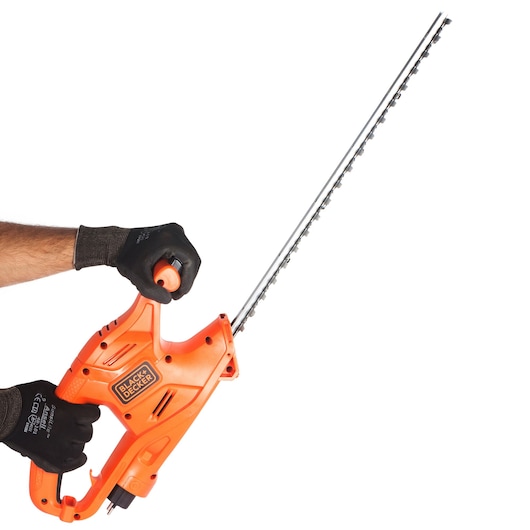 Photo of BLACK+DECKER GT4245 orange electric hedge trimmer, side angle, held by gloved hands.