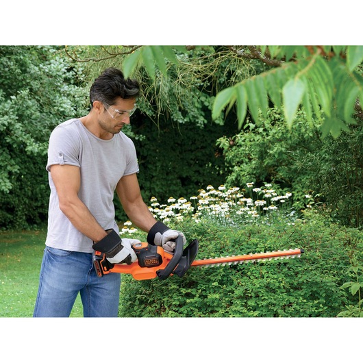 Photo of person trimming bushes with BLACK+DECKER hedge trimmer GTC18452PCB in a garden.
