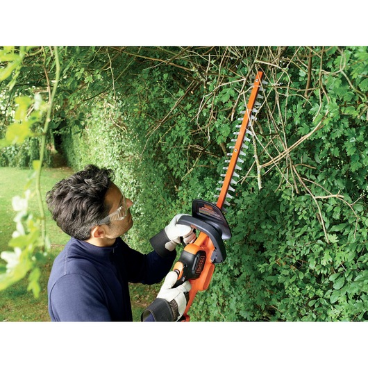 Photo of person using BLACKDECKER GTC18452PCB hedge trimmer on tall hedge outdoors.