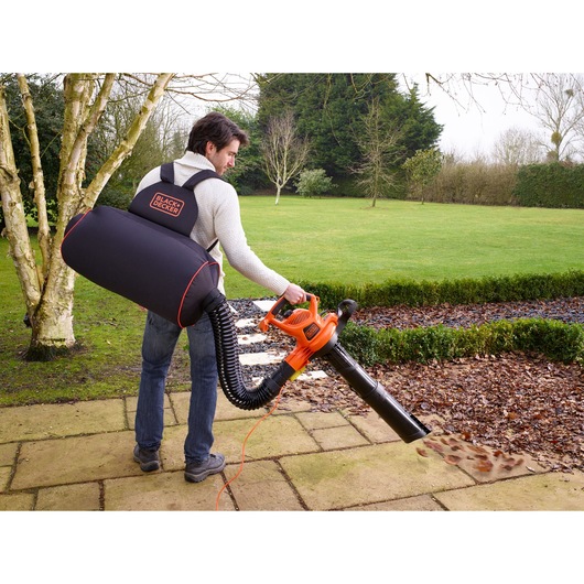 BLACK+DECKER GW3031BP leaf blower with large black collection bag used outdoors on garden path.