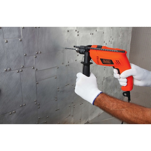 BLACKDECKER HD650 orange corded drill held by gloved hands drilling into a metal sheet, side angle.