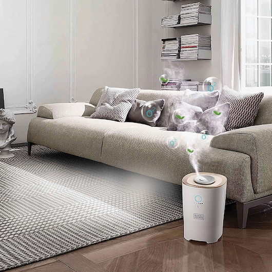 BLACK+DECKER HM4000 air purifier in white, releasing mist near a beige sofa in a modern living room.