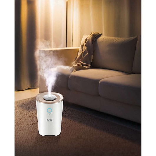 BLACK+DECKER HM4000 humidifier emitting mist in living room next to beige sofa on carpeted floor.