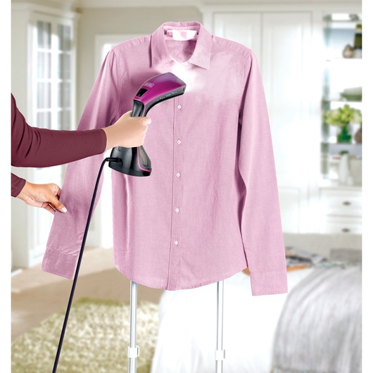 BLACKDECKER HSTD1600 handheld garment steamer in use on a pink shirt in a bedroom setting.