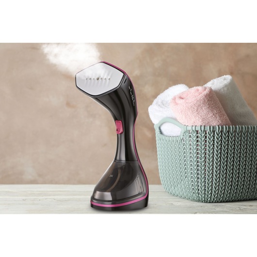 BLACKDECKER HSTD1600 handheld garment steamer emitting steam, next to a basket with rolled towels, front view.