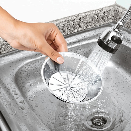 BLACK+DECKER JE780 juicer metal filter basket being rinsed under faucet in a stainless steel sink.