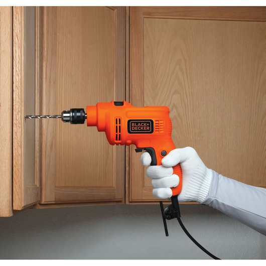 BLACKDECKER KR5010V corded orange drill used on wood cabinet, held by gloved hand.