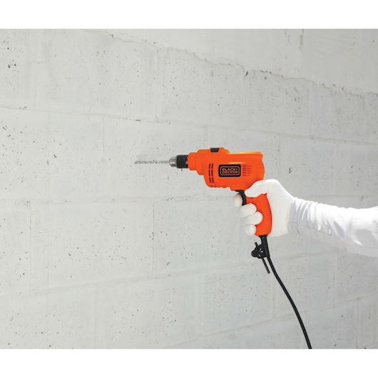 BLACKDECKER KR5010 orange corded drill held against white concrete wall, side view, power tool category.