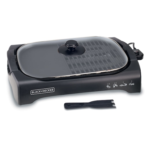 A BLACK+DECKER electric indoor grill with a glass lid and a black spatula placed in front. The grill has a control knob on the right side and illustrated cooking instructions on the front panel.