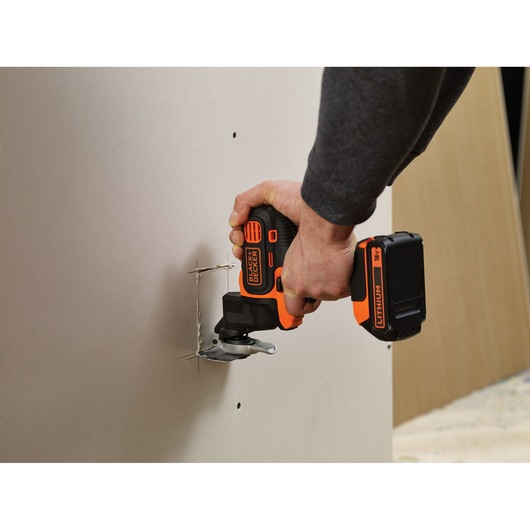 Photo of BLACKDECKER MT218K cordless oscillating tool cutting drywall, visible hand operation.