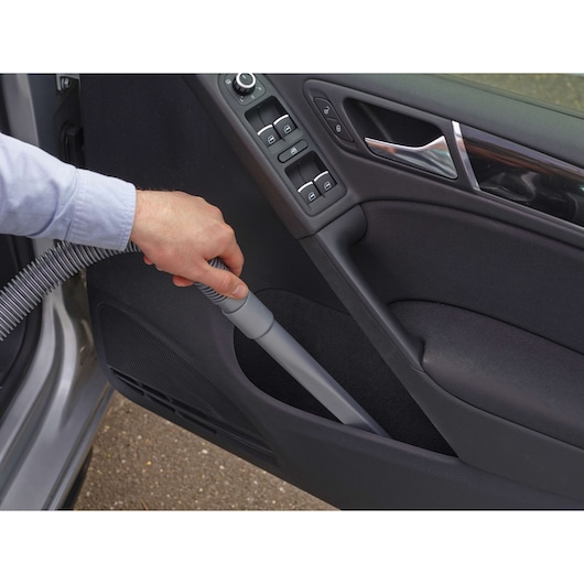 A person is using a vacuum cleaner with a narrow attachment to clean the inside door pocket of a car.