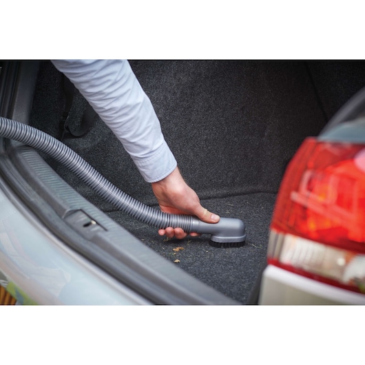 A person is using a handheld vacuum cleaner with a hose to clean the interior of a car trunk.