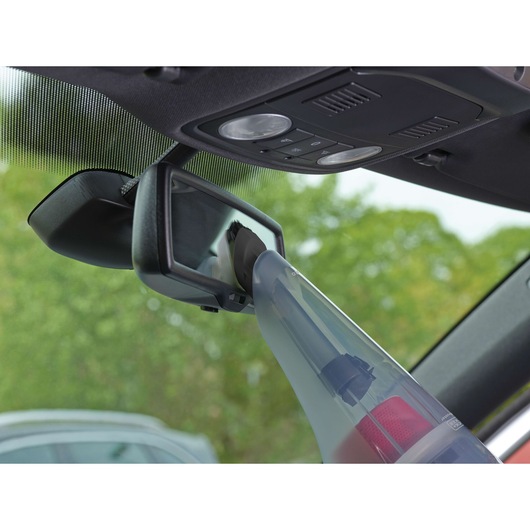 BLACKDECKER NV1210AV handheld vacuum cleaning a car rearview mirror, close-up interior angle.