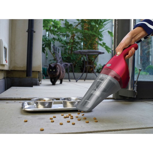 Photo of BLACKDECKER NVB115WA handheld vacuum cleaning pet food near metal bowls on a patio, black cat in background.