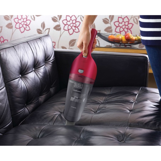 BLACK+DECKER NVB115WA handheld vacuum cleaner with red and grey design cleaning black leather sofa.
