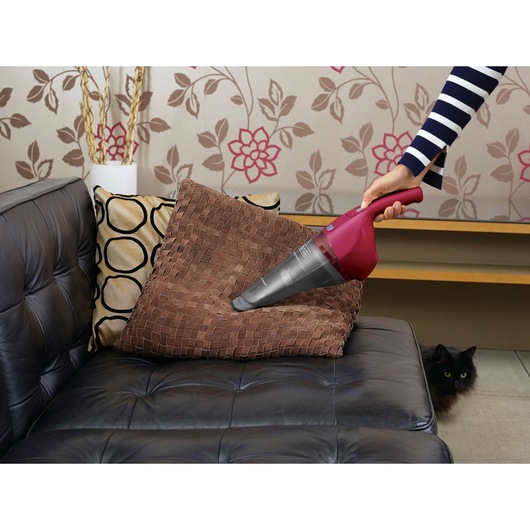 BLACK+DECKER NVB115WA handheld vacuum cleaning a brown cushion on a black leather sofa in a living room.
