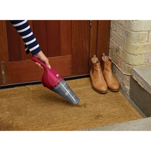 BLACK+DECKER NVB115WA handheld vacuum in red being used on a doormat near boots at a doorway.