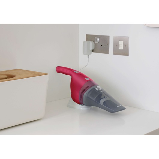 BLACK+DECKER NVB115WA cordless handheld vacuum in pink charging on white counter, side view.