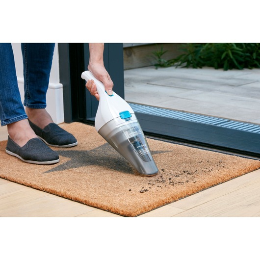 BLACKDECKER NVC115JL handheld vacuum cleaning debris from a brown doormat near an open door.