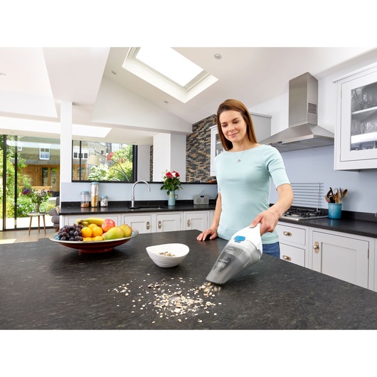 BLACKDECKER NVC115JL handheld vacuum cleaning spilled oats on kitchen counter near fruit bowl.