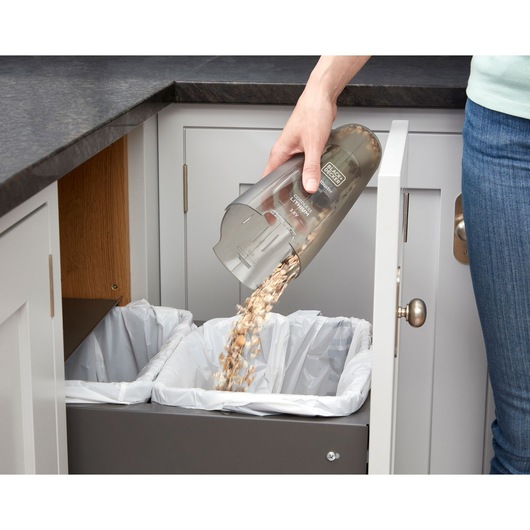 Photo of BLACK+DECKER NVC115JL handheld vacuum being emptied over kitchen trash bin, debris falling out.