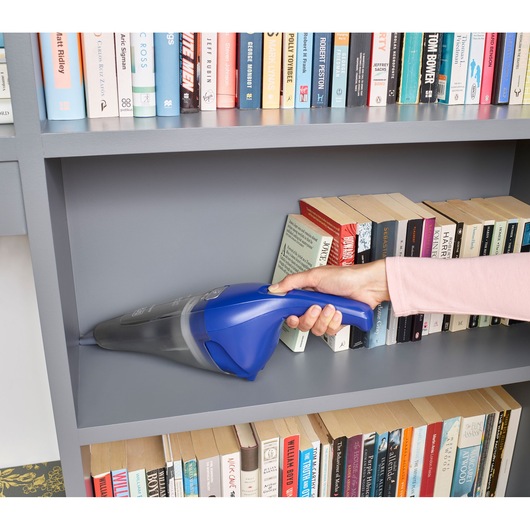 Photo of BLACKDECKER NVC115WA handheld vacuum cleaning a gray bookshelf with books.