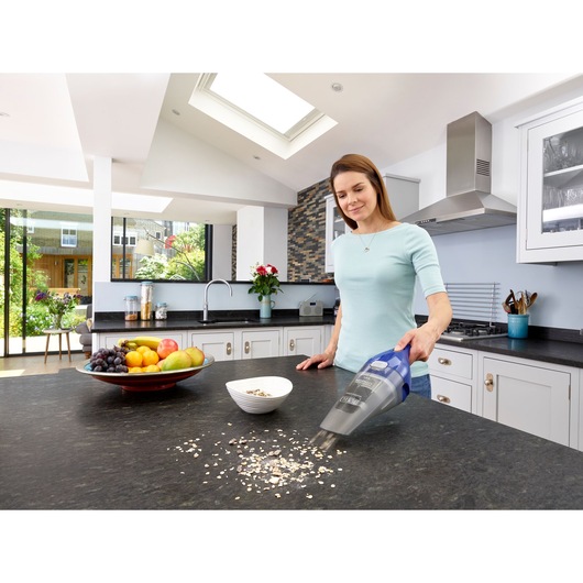 BLACK+DECKER NVC115WA handheld vacuum cleaning oats on kitchen counter near fruit bowl, side view.