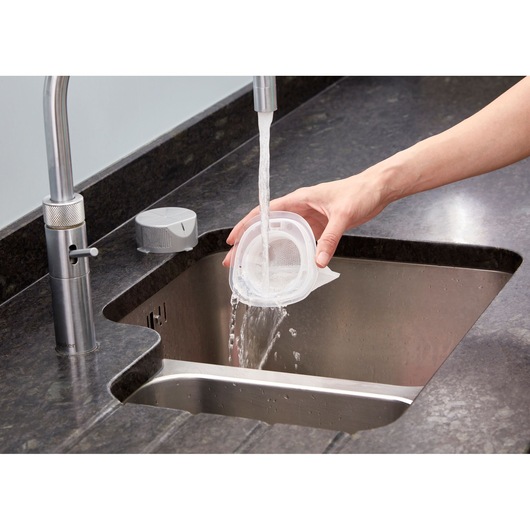 BLACKDECKER NVC115WA vacuum filter being rinsed under tap water in a kitchen sink, close-up angle.
