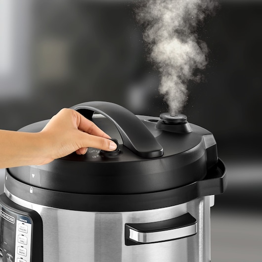 Photo of BLACKDECKER PCP1010 stainless steel pressure cooker with steam release, hand turning the valve, close-up.