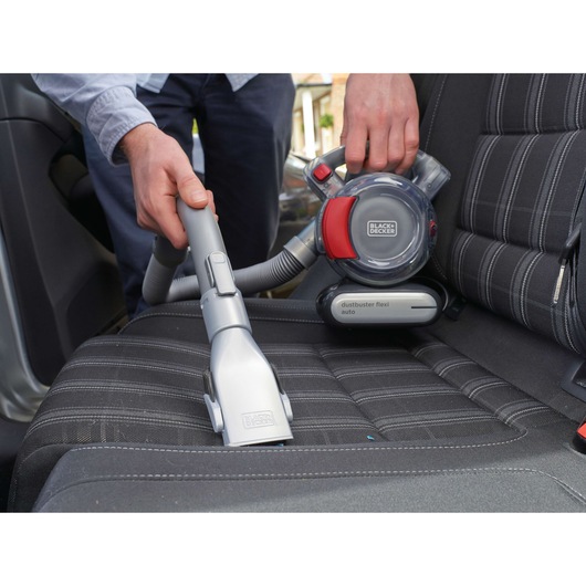 Photo of BLACKDECKER PD1200AV handheld vacuum cleaning a car seat, showing hose attachment and compact design.
