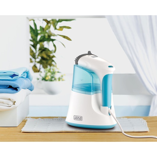 Photo of BLACK+DECKER PGST120 handheld garment steamer with white and blue design on a table, folded laundry beside.