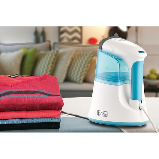 Photo of BLACK+DECKER PGST120 garment steamer with white and blue design, placed on a table next to folded clothes.