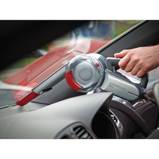 BLACK+DECKER PV1200AV handheld car vacuum with red and grey accents used for cleaning car dashboard.