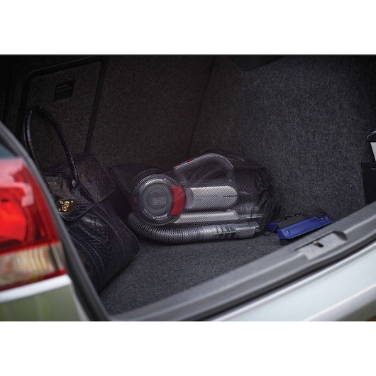 BLACKDECKER PV1200AV handheld vacuum cleaner stored in a car trunk, visible with accessories and bag.