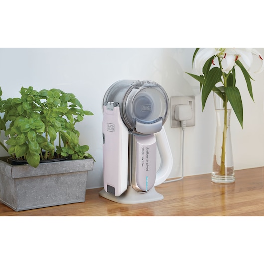 BLACK+DECKER PV1820LRGP handheld vacuum on charging base on kitchen counter, next to basil plant and vase with flowers.