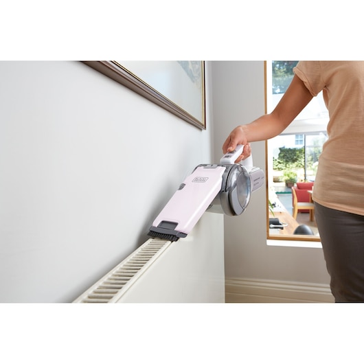 BLACK+DECKER PV1820LRGP handheld vacuum cleaning white radiator, person holding handle, indoor scene.
