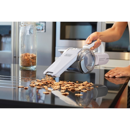 BLACKDECKER PV1820LRGP handheld vacuum cleaning cereal from kitchen counter, side angle.