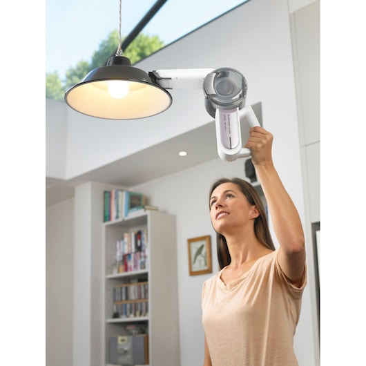 BLACK+DECKER PV1820LRGP handheld vacuum being used to clean a hanging lamp in a modern living room.