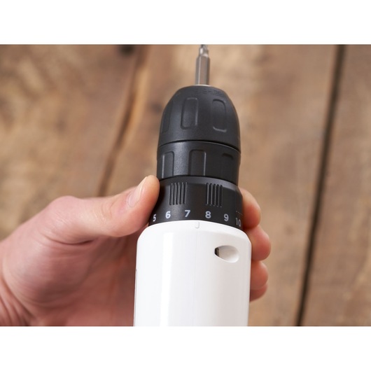 Close-up photo of BLACKDECKER REVDD12C cordless drill showing hand adjusting torque settings, wood background.