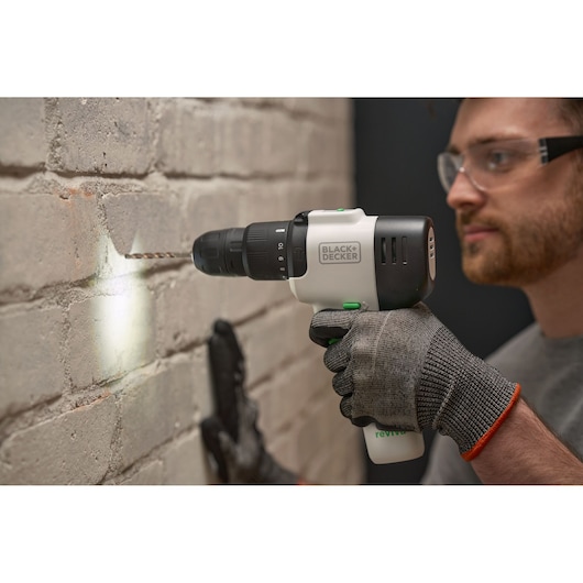 BLACK+DECKER REVHD12C cordless drill in use on brick wall, gloved hand holding handle.