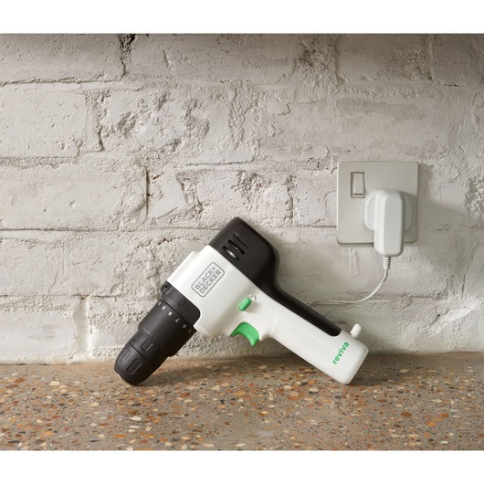 BLACKDECKER REVHD12C cordless drill with black and white body charging on countertop by white brick wall.