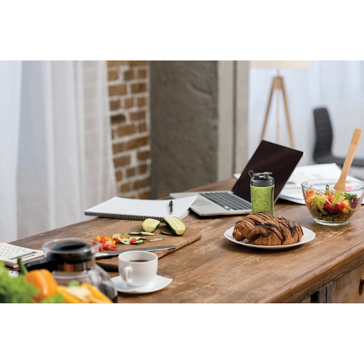BLACKDECKER SBX300 portable blender with green smoothie on a kitchen table with salad, croissant, and laptop.