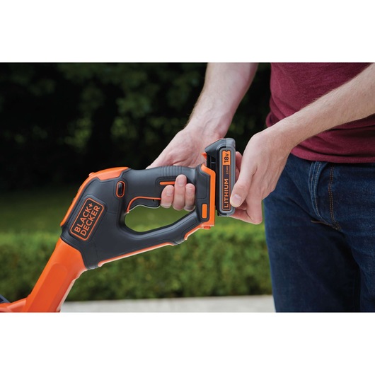 Close-up of BLACK+DECKER STC1820PCB garden tool handle with user inserting 18V lithium battery outdoors.