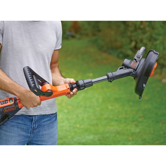 Photo of a person holding a BLACK+DECKER STC1820PCB cordless grass trimmer outside on green lawn.